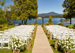 Outdoor wedding event near a lake with rows of white chairs.