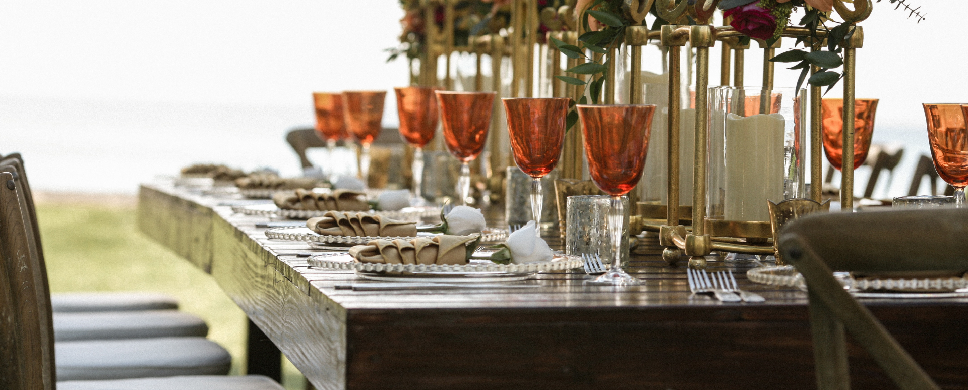A wood table at a special event set with orange wine glasses, candles, and flowers.