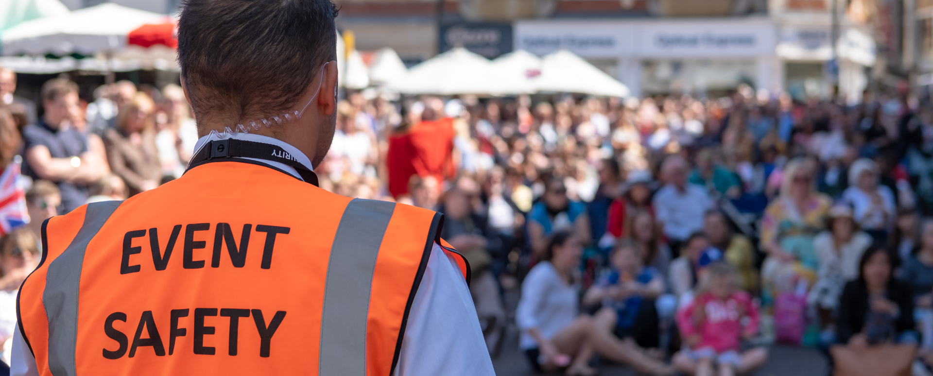 Man wearing an orange vest with event safety written on it as he controls crowds at an outdoor festival.