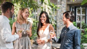 Four people stand outside smiling and drinking wine.