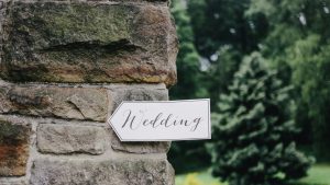 A white sign that says "wedding" is attached to a brick wall.