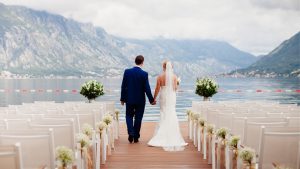 Man and woman stand on a wood dock overlooking a lake during their wedding ceremony.