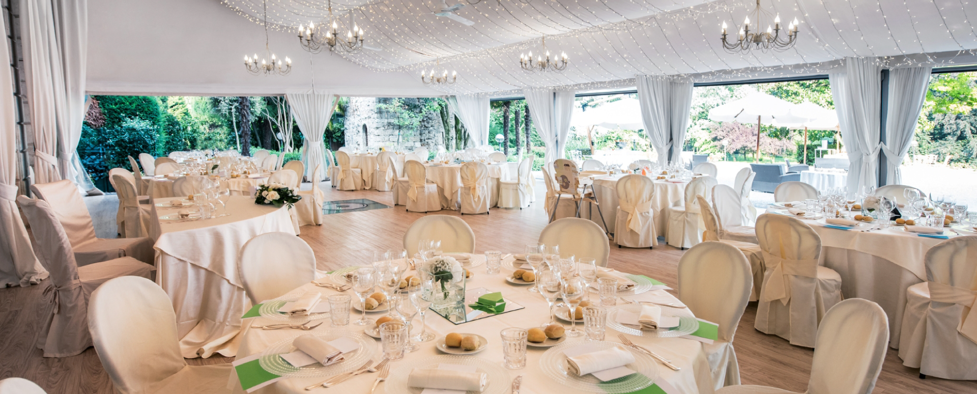 Wedding venue under a large white tent with chandeliers, round tables, white table cloths, and crystal glassware.