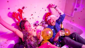 Two people wearing sparkly party clothes while laughing and sitting in a bathtub.
