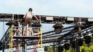 Man sets up scaffolding for an outdoor concert event.