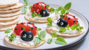 Party appetizers made from water crackers, cream cheese, and vegetables made to look like lady bugs.