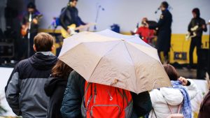 Three people standing under a beige umbrella.