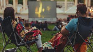 Two people sit in folding chairs watching a movie outdoors.