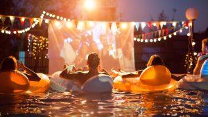 People at an outdoor event in the evening sitting in pool floaties watching a movie.