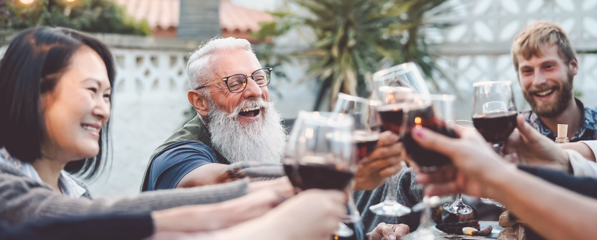 A group of friends laughing as they toast with wine glasses at an outdoor event.