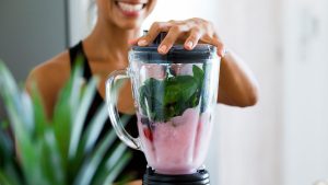 A woman mixes a smoothie with strawberries and spinach in a blender.