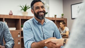 A bearded man in a blue shirt shakes hands with an insurance broker.