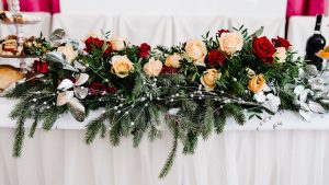 A table at a wedding with a white tablecloth and winter greenery and flowers on it.