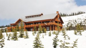 A two-story lodge on top of a snowy hill with evergreen trees.