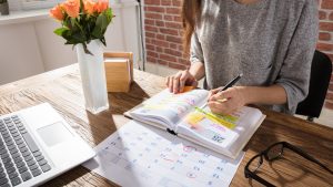 Woman in gray sweater sits a desk highlighting events in her personal calendar.