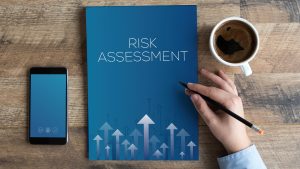 A blue book with the title "Risk Assessment" and a smartphone and coffee cup on a table.