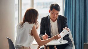 A man and a woman sit at a small white table reviewing paperwork.