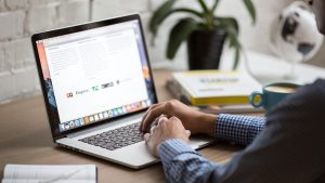 A man in a blue shirt types on his laptop.