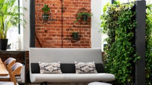 Contemporary seating area with living wall filled with greenery as well as an exposed brick wall, white couch, and wood table with gray chairs.