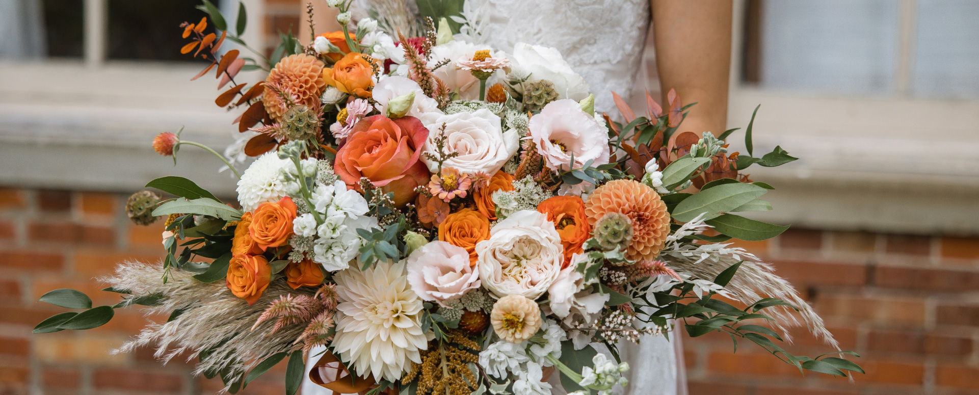 Bride holding large bouquet of flowers including orange and pale pink roses, dahlias, baby's breath, and more.