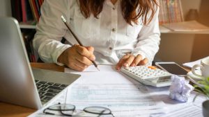 Woman sitting at desk with pencil, paper, calculator, and laptop.