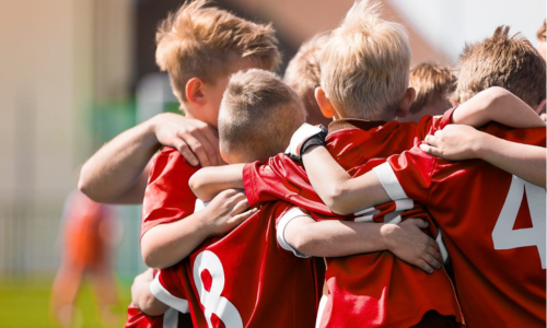 kids-soccer-team Six kids in a team huddle wearing red jerseys.
